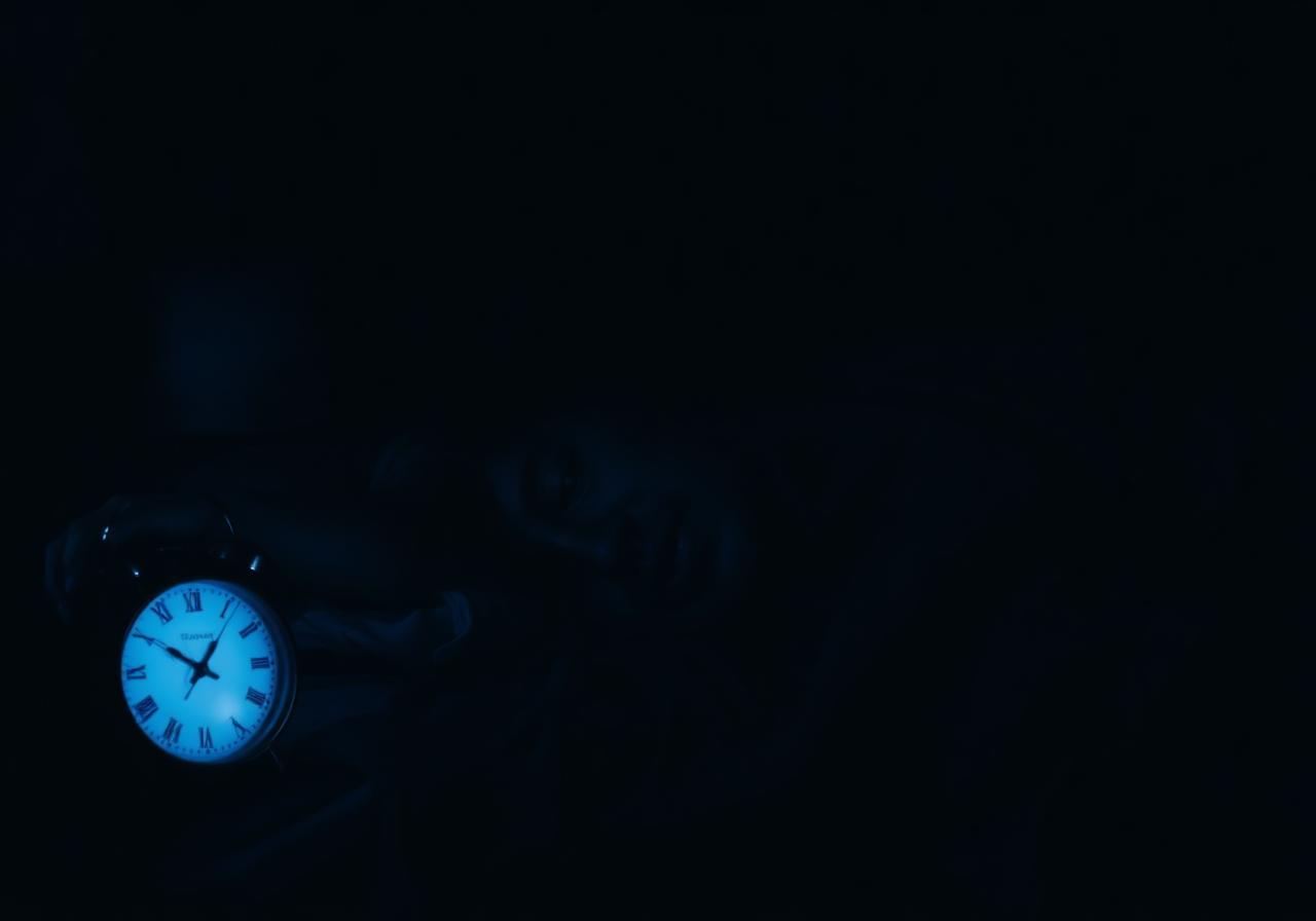 Man lying awake in a dark bedroom next to a glowing 11pm clock